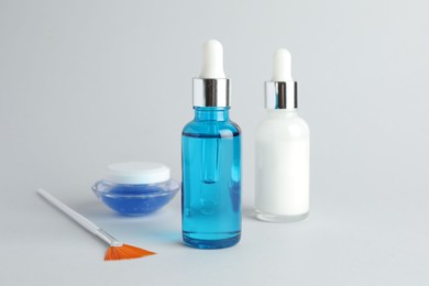 Photo of Bottles of chemical peel, jar and brush on light background. Peeling procedure