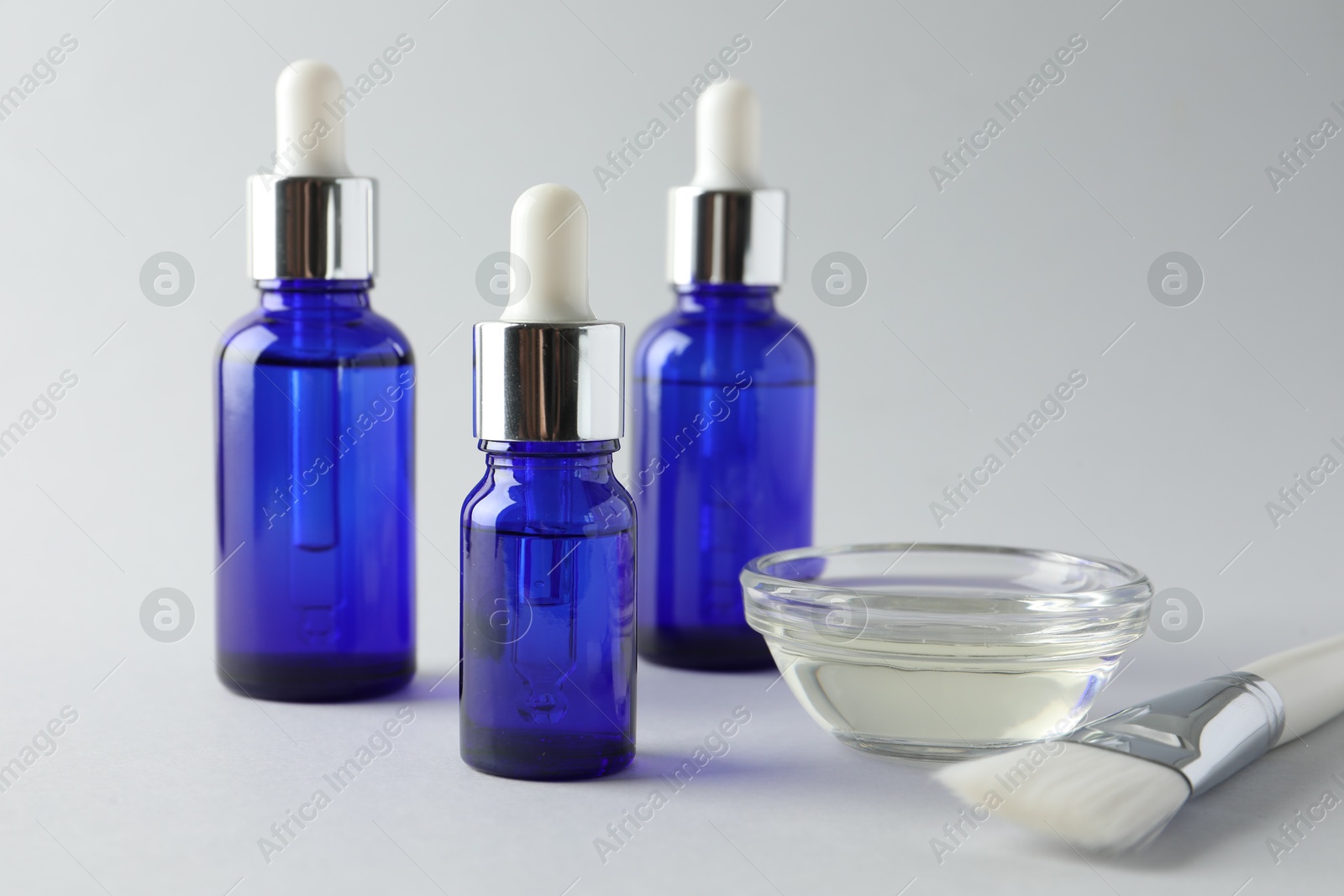 Photo of Bottles of chemical peel, bowl with liquid and brush on light background, closeup. Peeling procedure