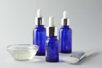 Photo of Bottles of chemical peel, bowl with liquid and brush on light background, closeup. Peeling procedure