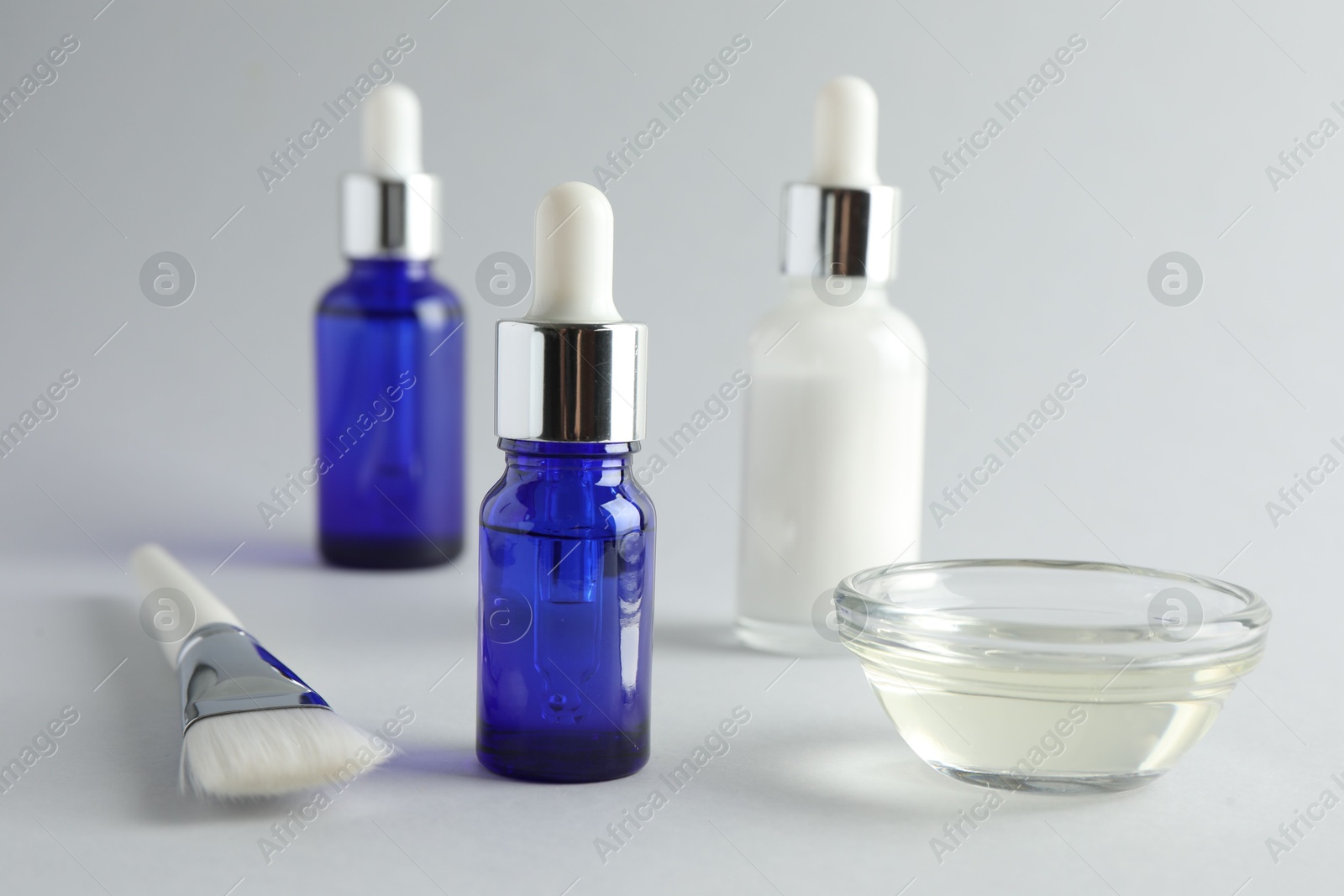 Photo of Bottles of chemical peel, bowl with liquid and brush on light background, closeup. Peeling procedure