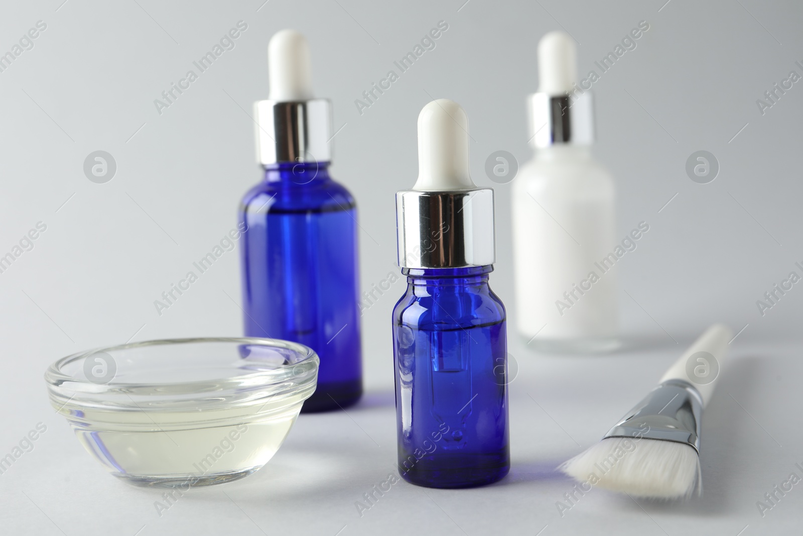 Photo of Bottles of chemical peel, bowl with liquid and brush on light background, closeup. Peeling procedure