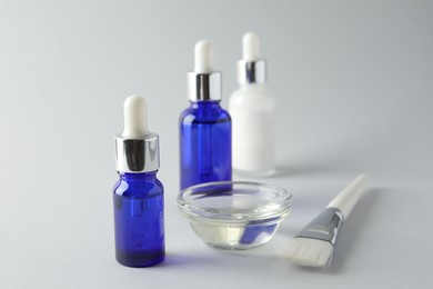 Photo of Bottles of chemical peel, bowl with liquid and brush on light background, closeup. Peeling procedure