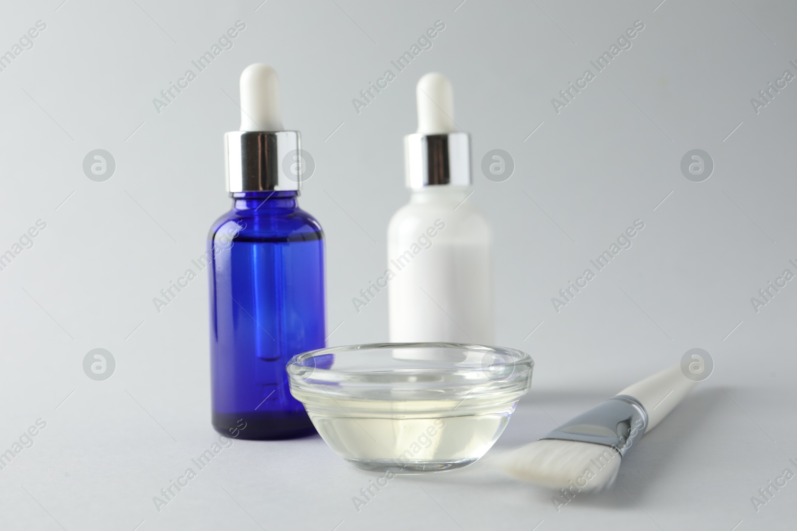 Photo of Bottles of chemical peel, bowl with liquid and brush on light background, closeup. Peeling procedure