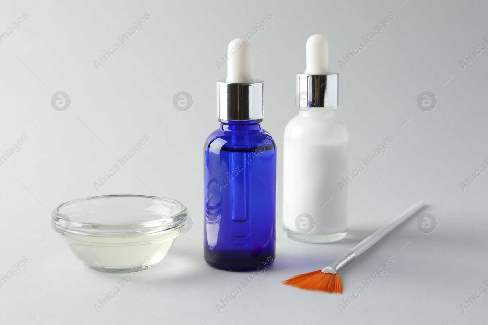 Photo of Bottles of chemical peel, bowl with liquid and brush on light background, closeup. Peeling procedure