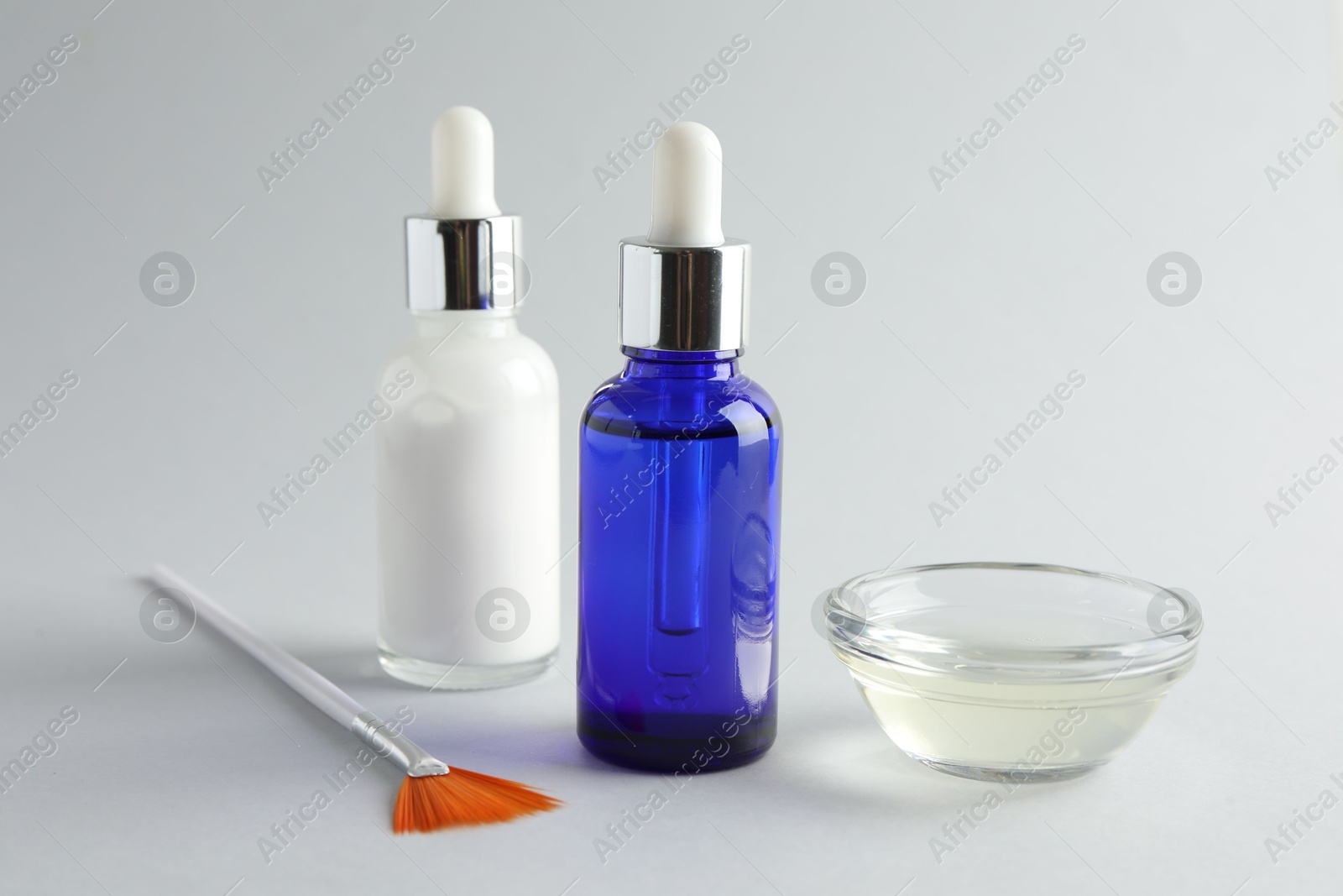 Photo of Bottles of chemical peel, bowl with liquid and brush on light background, closeup. Peeling procedure