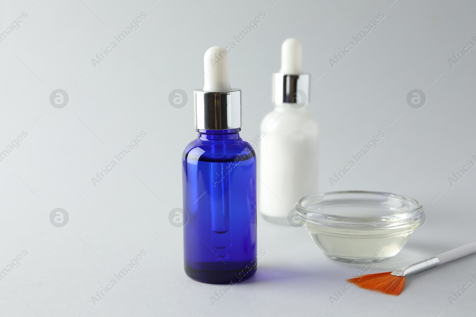 Photo of Bottles of chemical peel, bowl and brush on light background, closeup. Peeling procedure