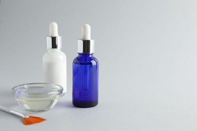 Photo of Bottles of chemical peel, bowl with liquid and brush on light background, space for text. Peeling procedure