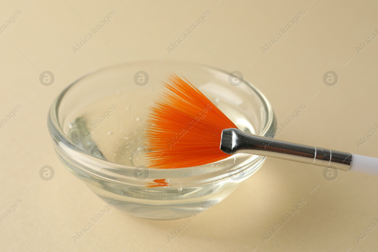 Photo of Chemical peel liquid in bowl and brush on beige background, closeup. Peeling procedure