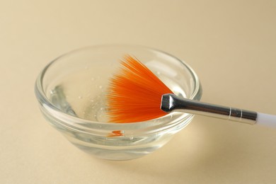 Photo of Chemical peel liquid in bowl and brush on beige background, closeup. Peeling procedure