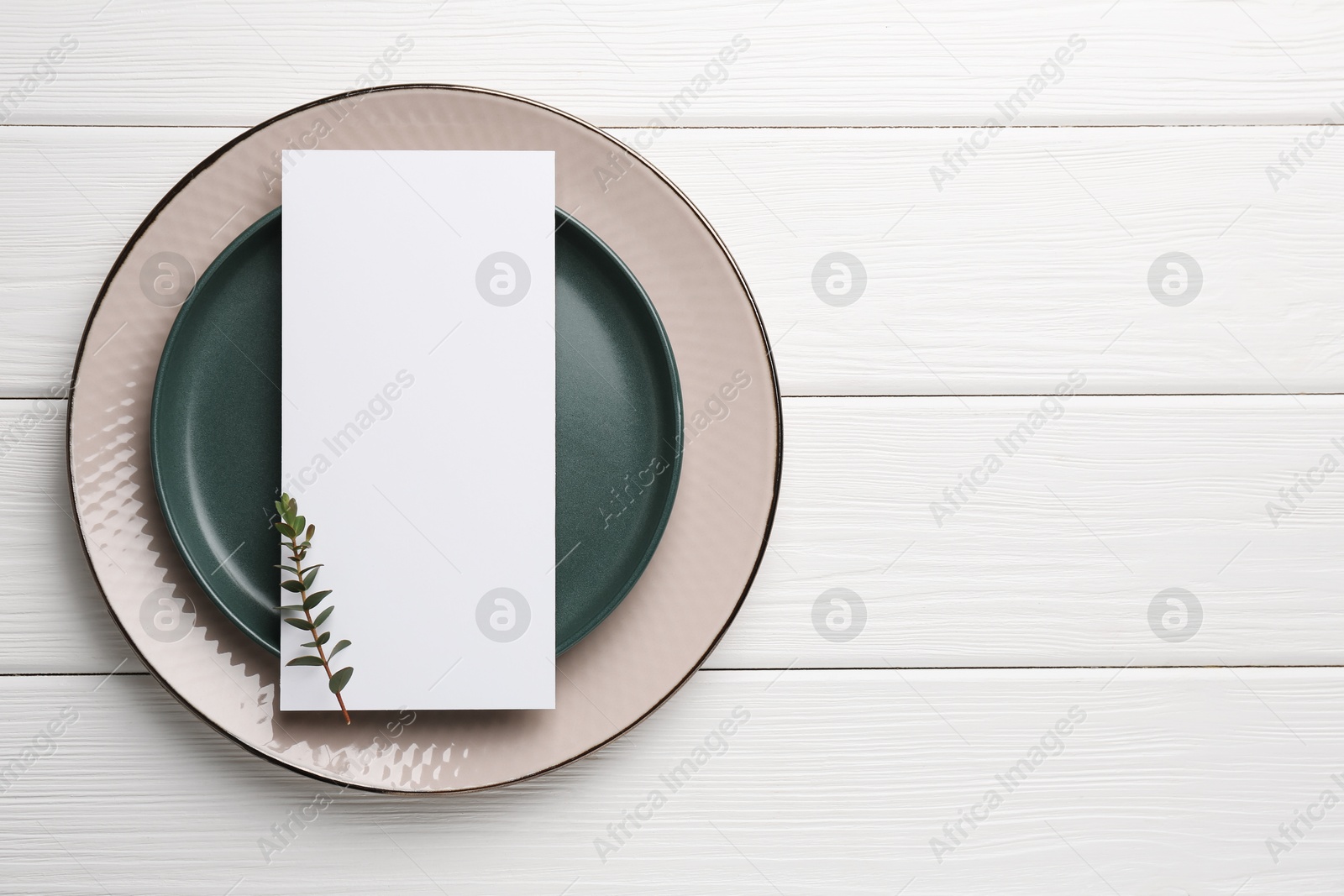 Photo of Empty menu, plates and floral decor on white wooden table, top view. Mockup for design