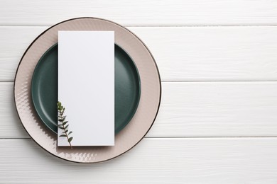 Empty menu, plates and floral decor on white wooden table, top view. Mockup for design