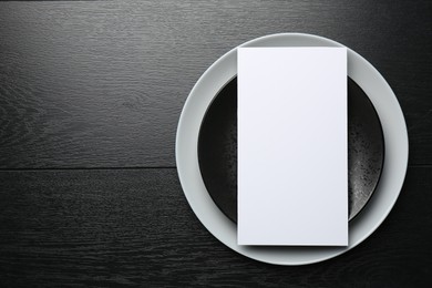 Empty menu and plates on black wooden table, top view. Mockup for design