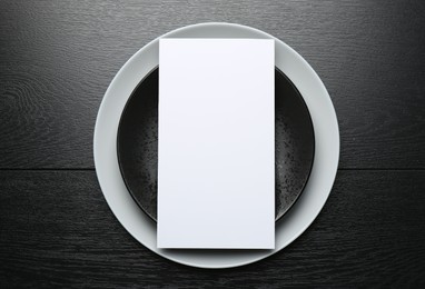 Photo of Empty menu and plates on black wooden table, top view. Mockup for design