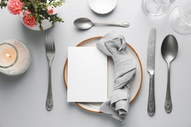 Photo of Empty menu, tableware, candle and floral decor on light grey table, flat lay. Mockup for design