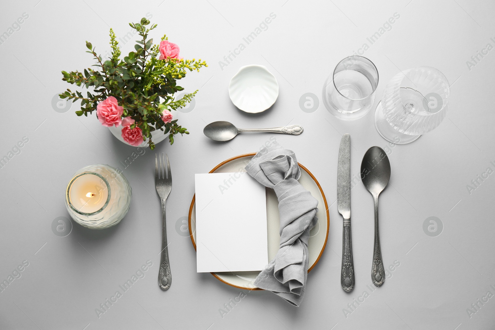 Photo of Empty menu, tableware, candle and floral decor on light grey table, flat lay. Mockup for design