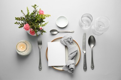 Empty menu, tableware, candle and floral decor on light grey table, flat lay. Mockup for design