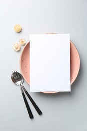 Photo of Empty menu, plate, cutlery and flowers on light grey background, top view. Mockup for design