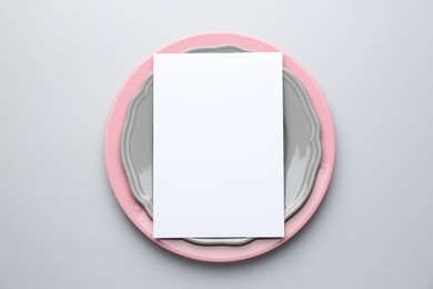 Photo of Empty menu and plates on light grey background, top view. Mockup for design