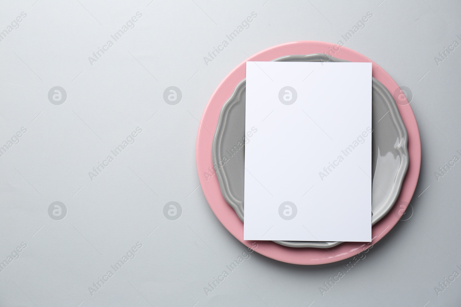 Photo of Empty menu and plates on light grey background, top view. Mockup for design