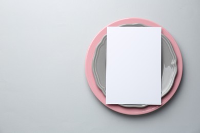 Empty menu and plates on light grey background, top view. Mockup for design