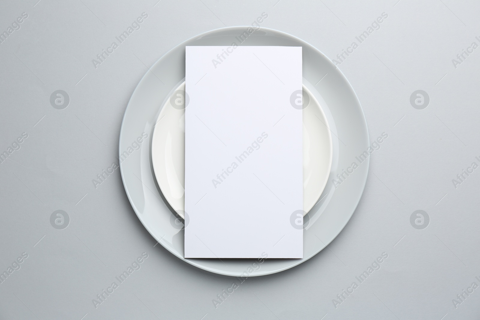 Photo of Empty menu and plates on light grey background, top view. Mockup for design