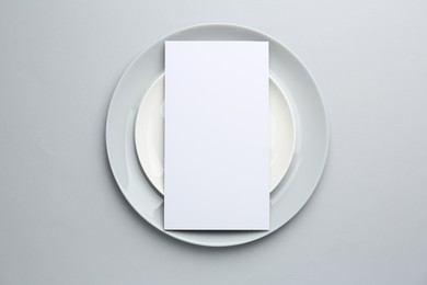 Empty menu and plates on light grey background, top view. Mockup for design