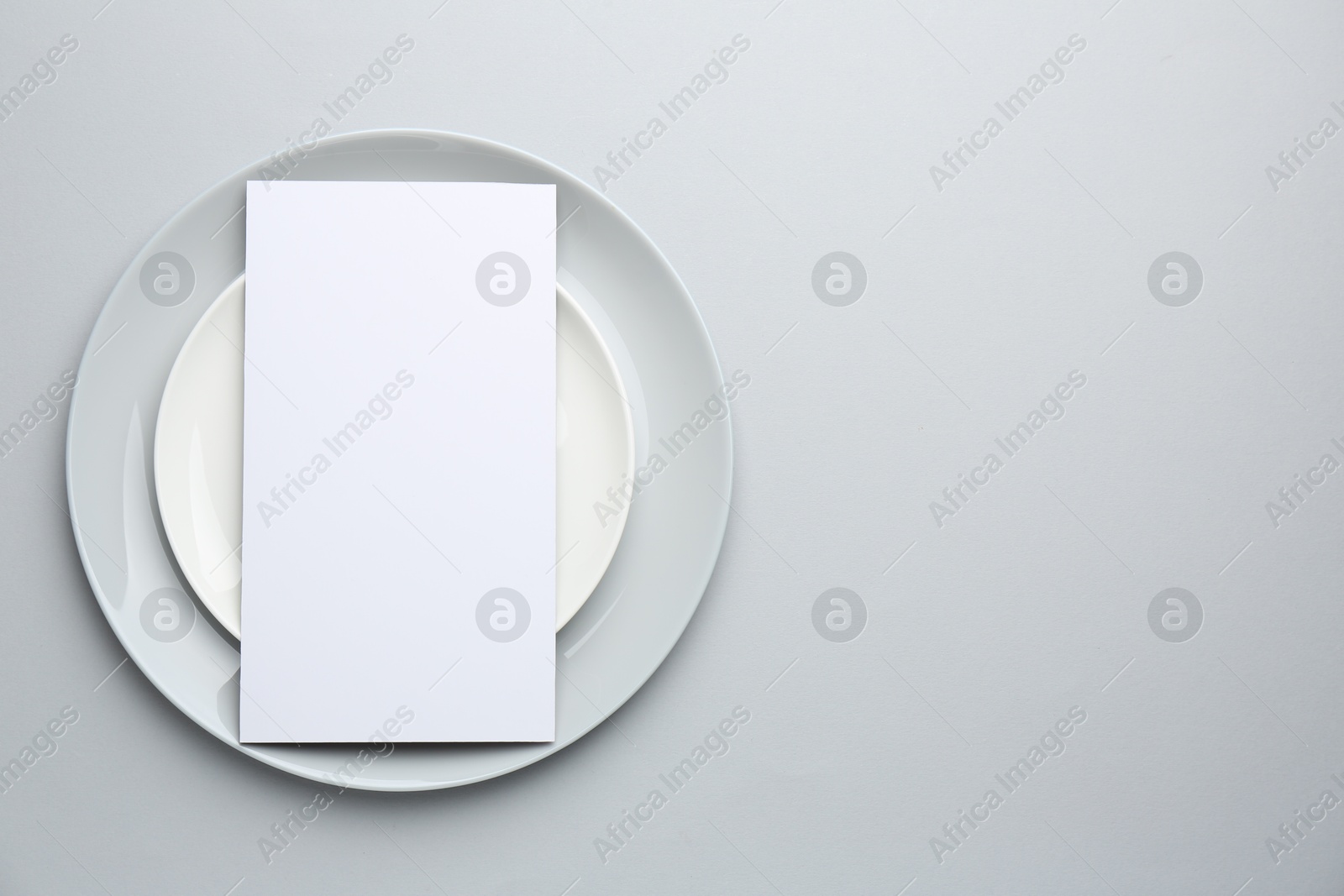 Photo of Empty menu and plates on light grey background, top view. Mockup for design