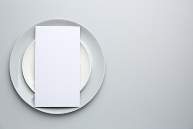 Photo of Empty menu and plates on light grey background, top view. Mockup for design