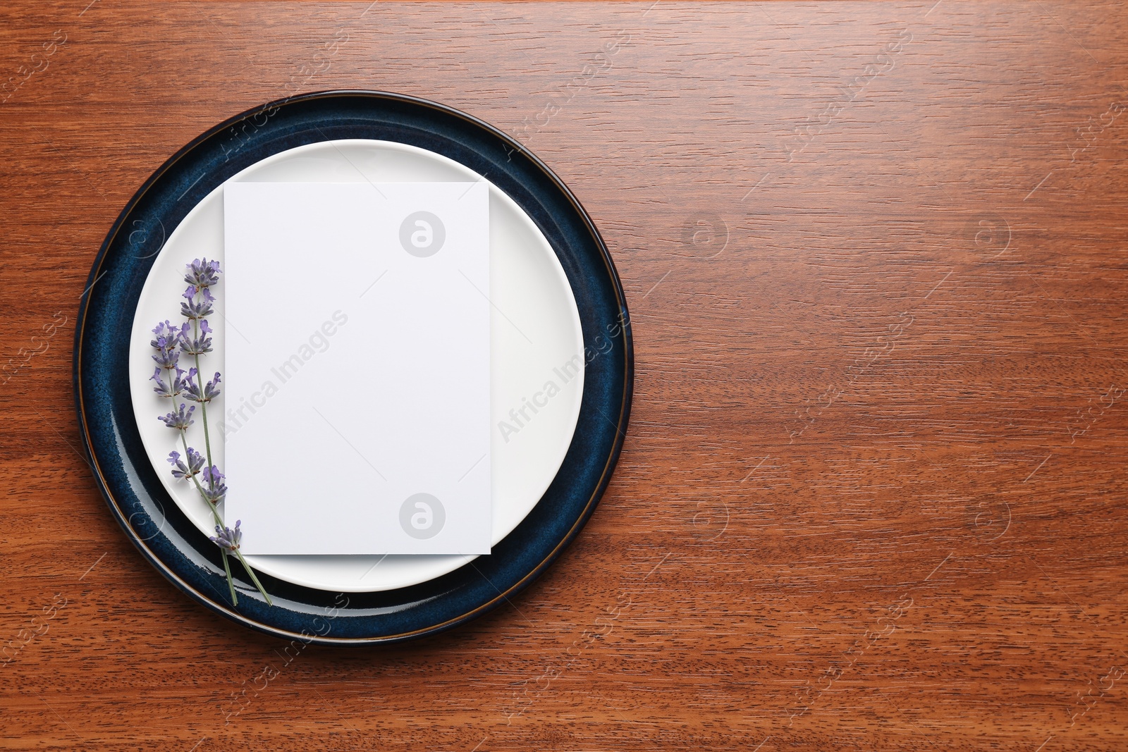 Photo of Empty menu, plates and floral decor on wooden table, top view. Mockup for design