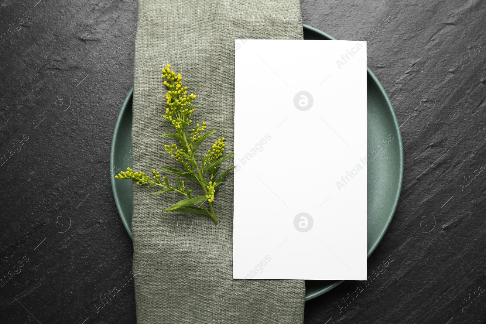 Photo of Empty menu, plate, napkin and floral decor on black table, top view. Mockup for design