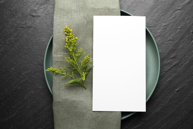 Photo of Empty menu, plate, napkin and floral decor on black table, top view. Mockup for design