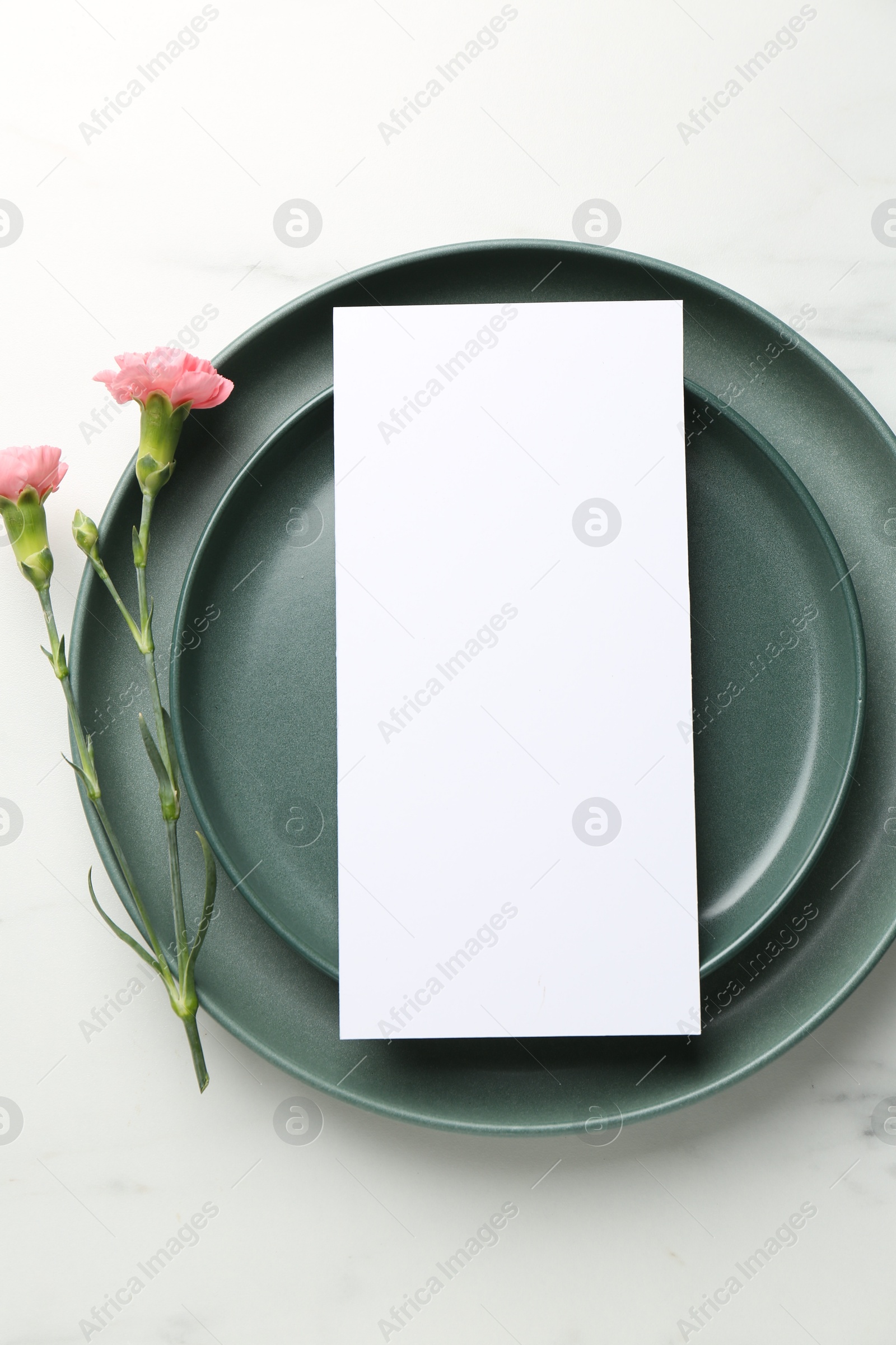 Photo of Empty menu, plates and floral decor on white marble table, top view. Mockup for design