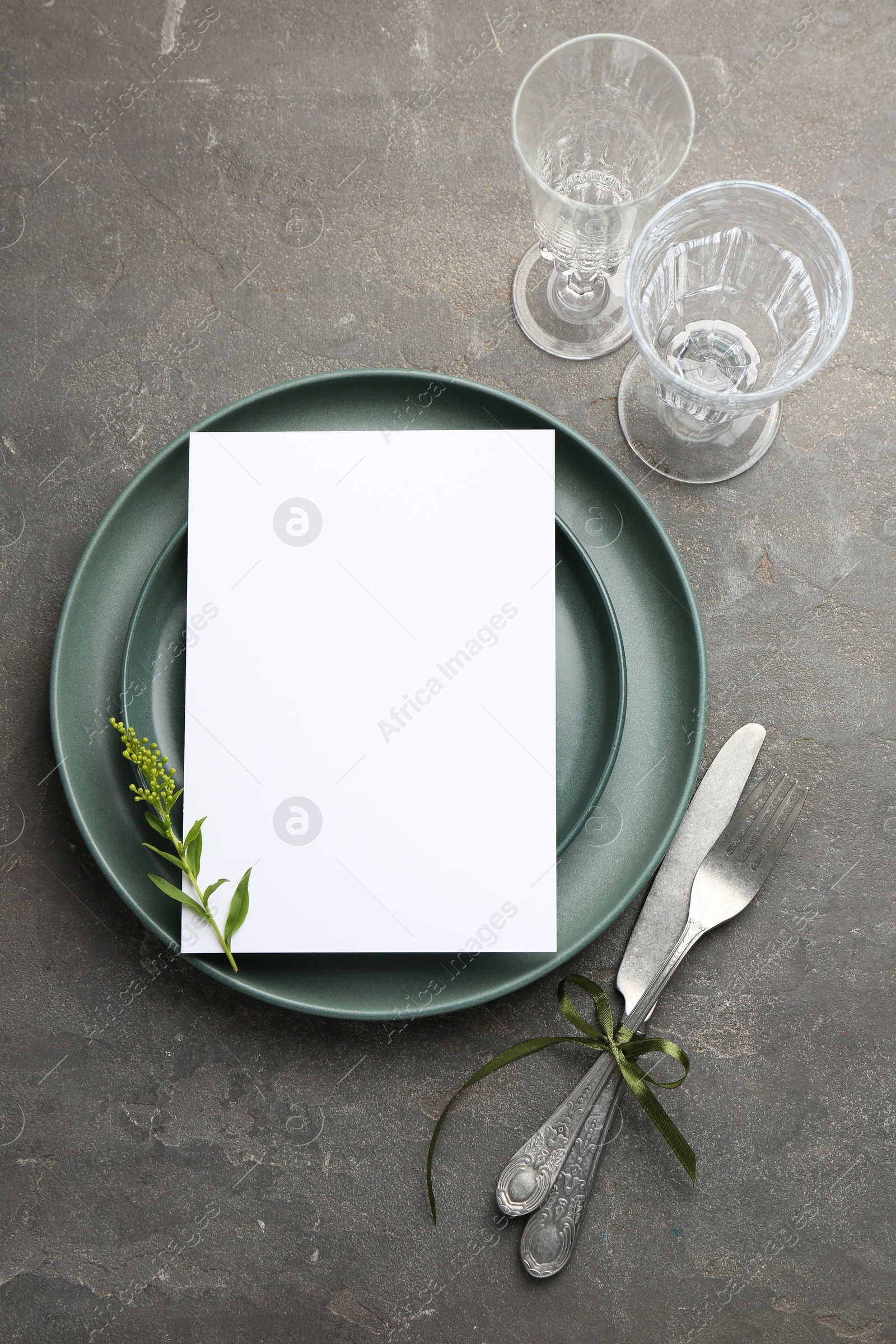 Photo of Empty menu, plates, cutlery, glasses and floral decor on grey table, top view. Mockup for design