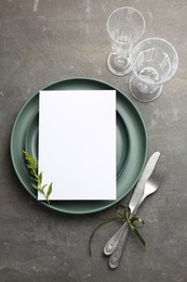 Empty menu, plates, cutlery, glasses and floral decor on grey table, top view. Mockup for design