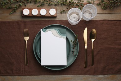 Photo of Empty menu, plates, cutlery, glasses and decor on wooden table, top view. Mockup for design