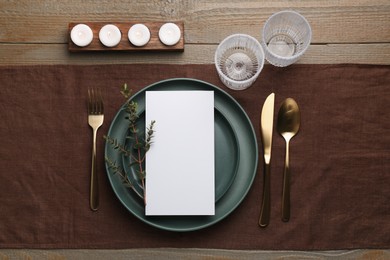 Empty menu, plates, cutlery, glasses and decor on wooden table, top view. Mockup for design