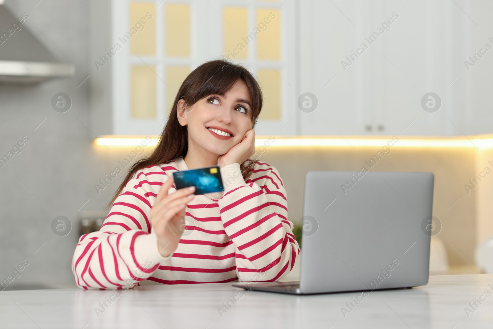 Photo of Online banking. Smiling woman with credit card and laptop paying purchase at table indoors