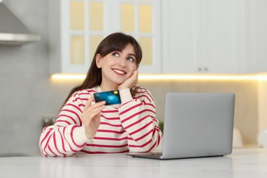 Online banking. Smiling woman with credit card and laptop paying purchase at table indoors