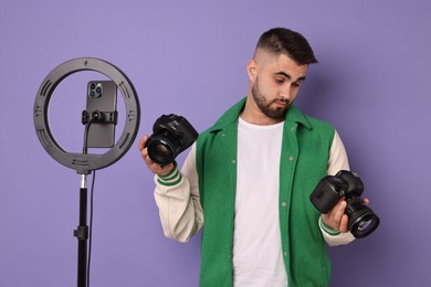 Photo of Technology blogger reviewing cameras and recording video with smartphone and ring lamp on purple background