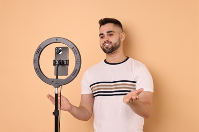 Photo of Blogger recording video with smartphone and ring lamp on beige background