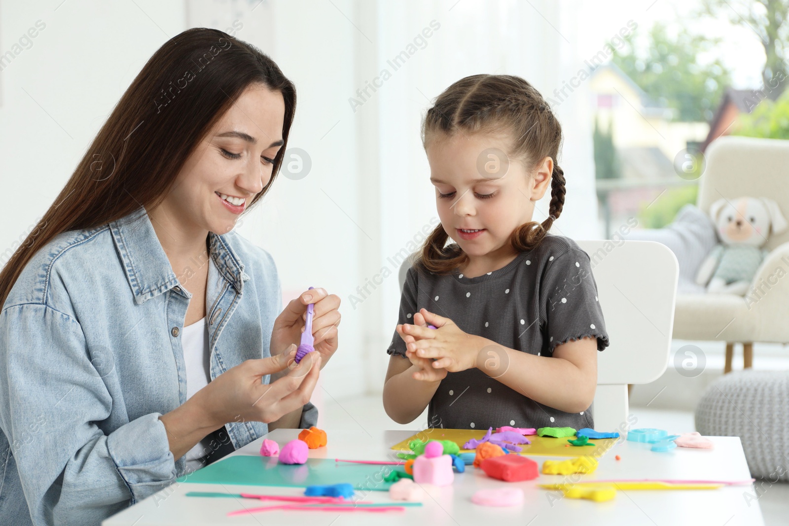 Photo of Smiling mother and her daughter sculpting with play dough at table indoors