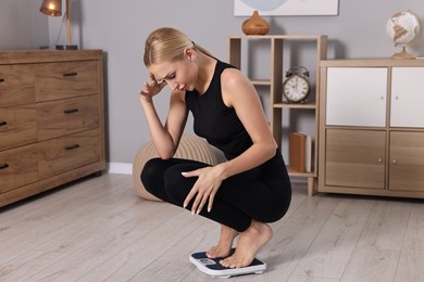 Worried woman on floor scale at home