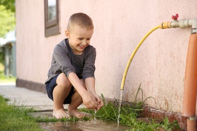 Photo of Water scarcity. Cute little boy drawing water with hands from tap outdoors