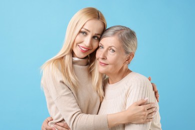 Family portrait of young woman and her mother on light blue background