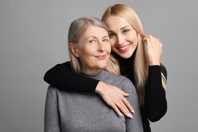 Family portrait of young woman and her mother on grey background