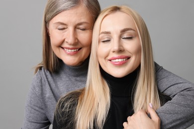 Family portrait of young woman and her mother on grey background