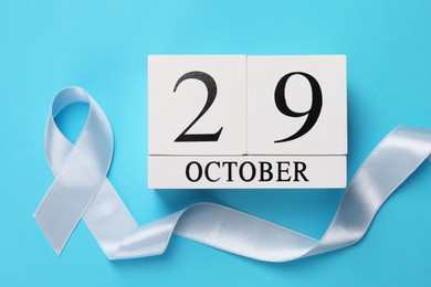 Photo of International Psoriasis Day - 29th of October. Block calendar and ribbon as symbol of support on light blue background, flat lay