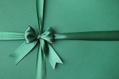 Bright satin ribbon with bow on green background, top view