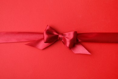 Photo of Bright satin ribbon with bow on red background, top view