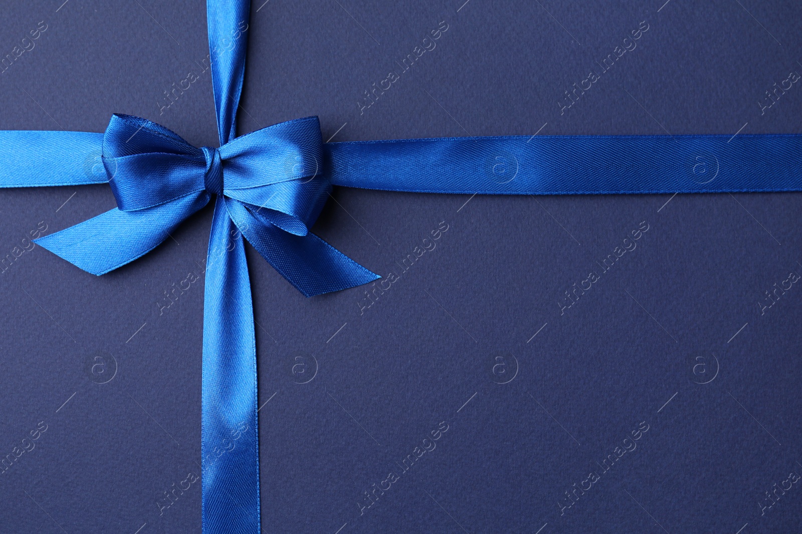 Photo of Bright satin ribbon with bow on blue background, top view